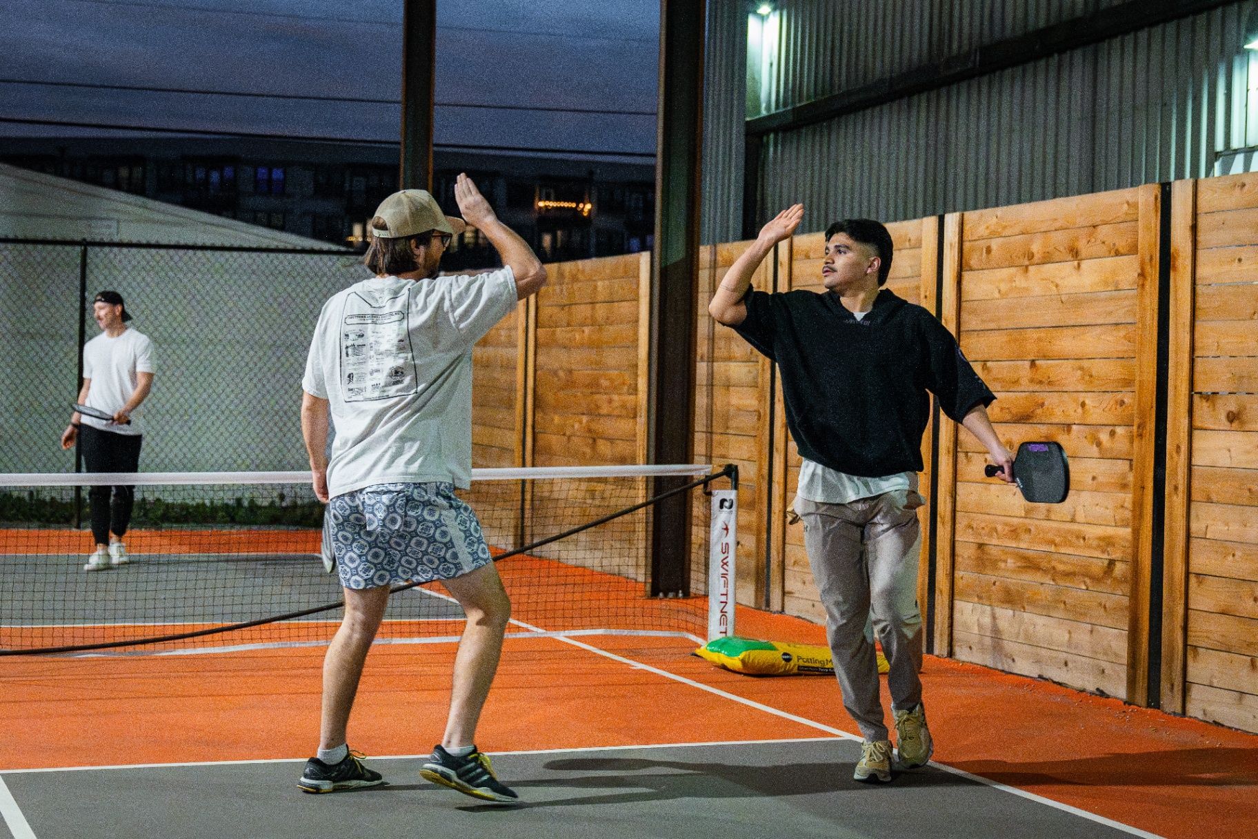 Teammates high-five at dusk between courts
